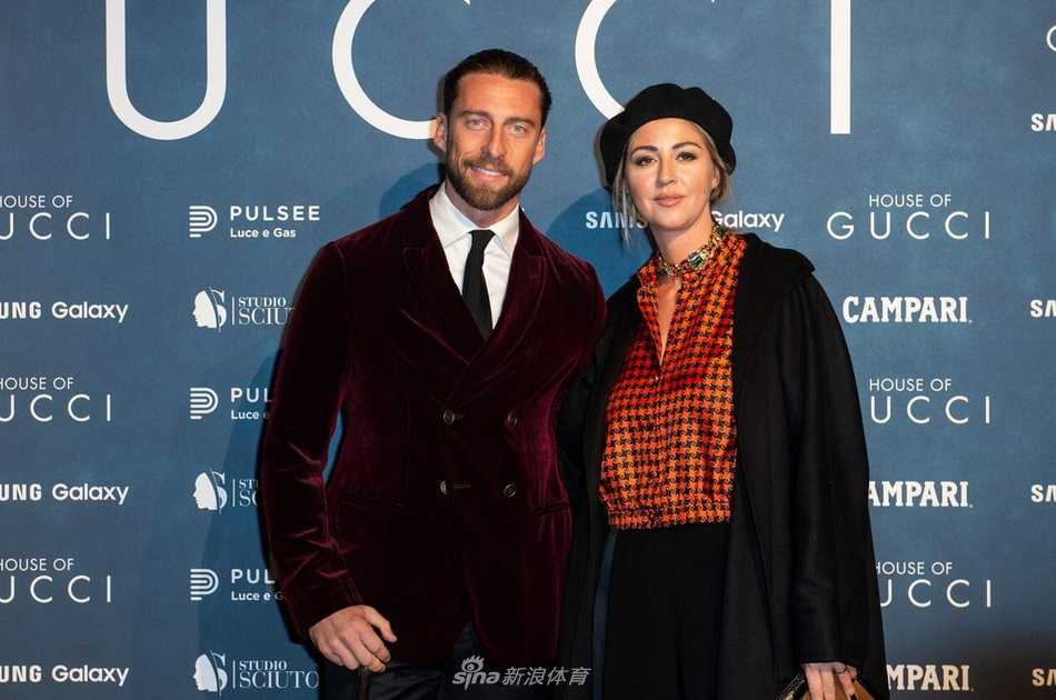 特写镜头捕捉到马尔基西奥与罗贝塔的温情瞬间，他微微侧身，温柔地注视着一旁正在签名的妻子，眼神中满是骄傲与爱意，罗贝塔则手持金色签名笔，专注而优雅，两人手腕上的精致饰品在灯光下闪烁