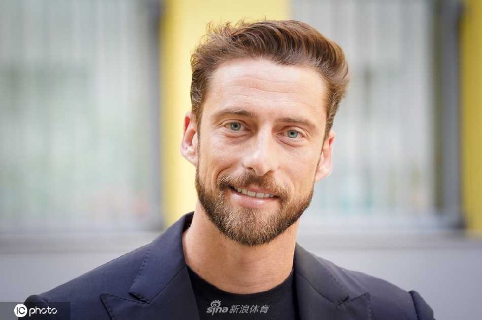 马尔基西奥在活动背景板前从容站立，双手自然下垂，身姿如松，展现出自信沉稳的公众人物风范。