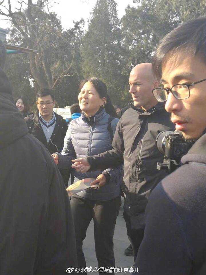 齐达内微微俯下身子，眼神专注而柔和，正在一张卡片上为热情的球迷签名。周围的人群虽然兴奋，却保持着礼貌的距离，记录下这位巨星毫无架子的暖心瞬间。