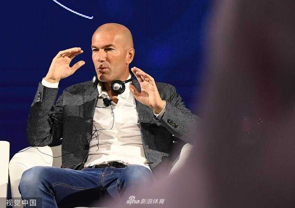 法国传奇球星齐达内西装革履现身迪拜会议中心，神情专注地聆听台上关于人工智能的演讲，背景是科技感十足的会议大屏