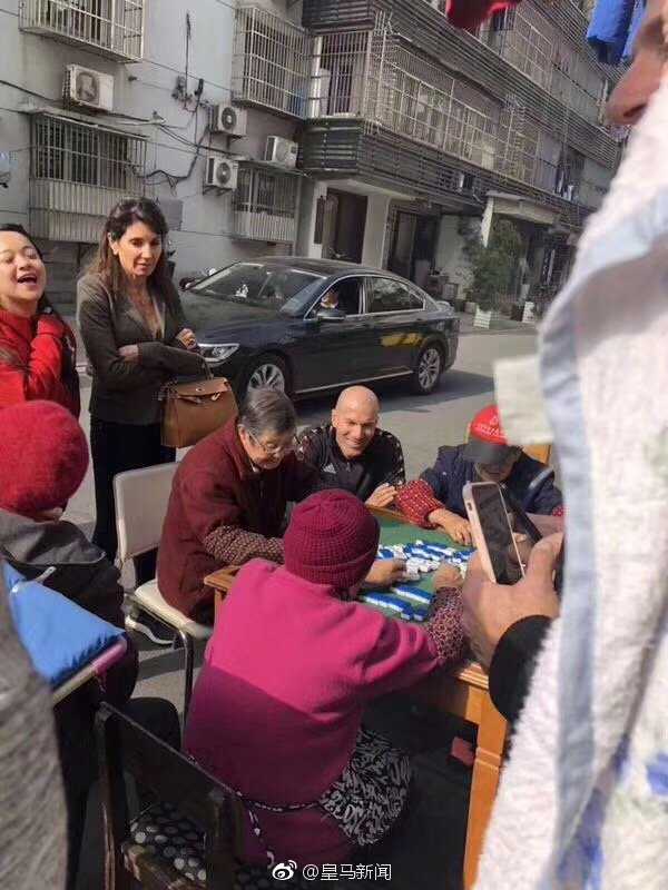 镜头拉近，齐达内坐在红色小板凳上身体微微前倾，脸上带着天真而慈祥的笑容，仿佛真的看懂了眼前的“长条”游戏。