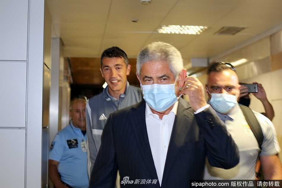 几名球员合力从大巴行李舱中搬出装满训练装备的橙色大包，汗水已经浸湿了他们的训练服后背，展现出职业球员的团队协作精神