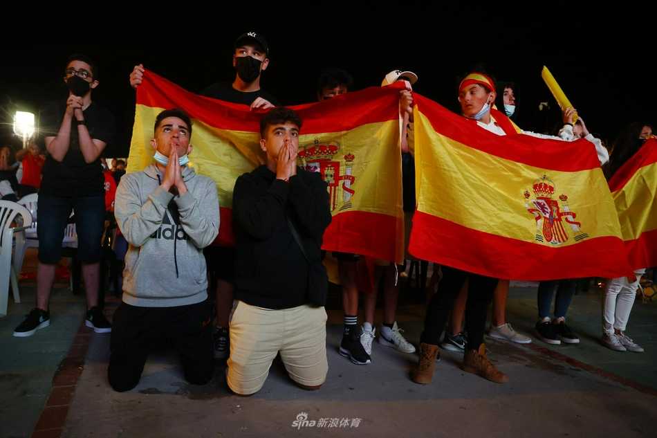fervor en la plaza el pequeño pueblo español se arrodilla por la victoria en la semifinal de la eurocopa La marea roja de Griñón llena la plaza al atardecer, con banderas y bufandas, creando un vibrante mosaico de pasión y esperanza antes del pitido inicial.