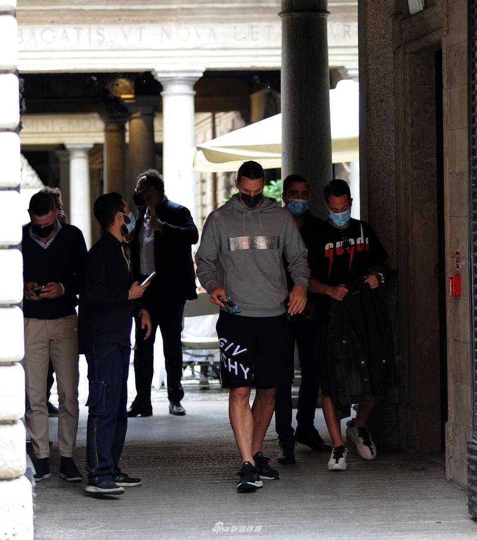 从侧面捕捉到的画面，伊布难得地露出了腼腆的笑容，阿巴特戴着棒球帽，侧脸轮廓分明，两人并肩站立，仿佛时间在他们身上定格，身后是米兰春日的葱郁绿植。
