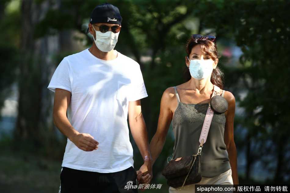 齐达内身穿简约的白色T恤，与穿着碎花长裙的妻子维罗妮卡漫步在伊比萨岛的街头。阳光洒在他们身上，两人紧紧相依，十指如同初恋般牢牢相扣，脸上洋溢着宁静而满足的微笑，仿佛整个世界都与他们无关。