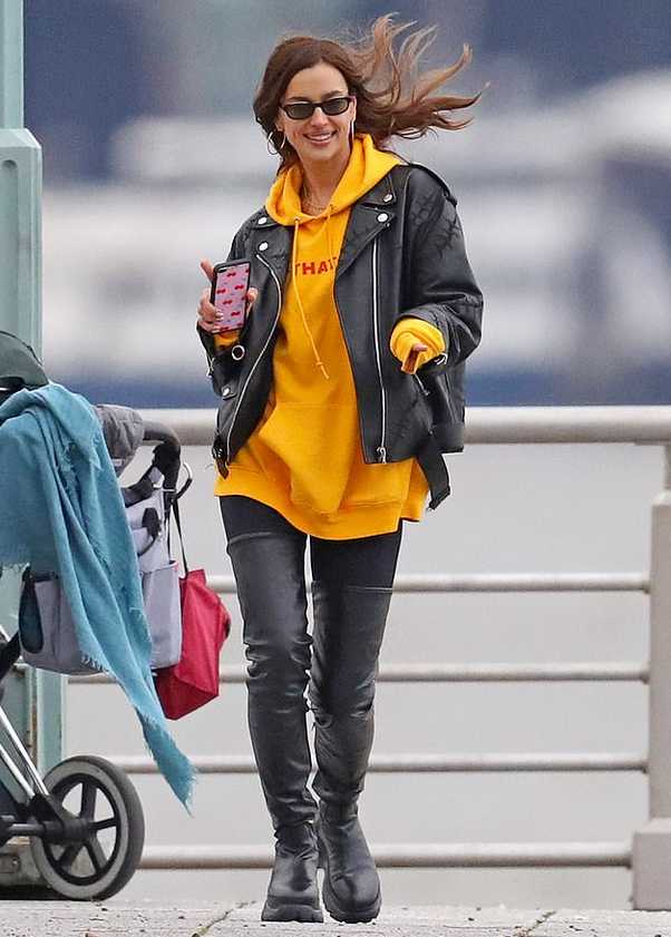 伊莲娜单手抱着女儿，步伐带风尽显超模气场，而怀里的小莉娅则淡定地嘬着手指，一副“本宝宝早已习惯这种大场面”的从容神态。