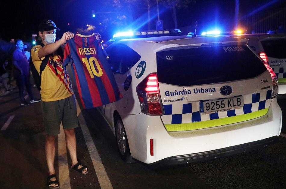 夜幕低垂，人群依然没有散去的意思。一名安保人员双手背后，笔直地站在诺坎普一处入口的铁门前，他的身后是灯火通明却空无一人的球场，身前则是密密麻麻、神情殷切的人群，这道铁门隔开了两个截然不同的世界。