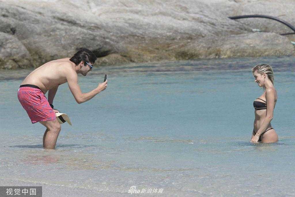 卡洛琳娜身穿黑色深V高叉泳装，从海中走上沙滩，健康的身材曲线毕露，卡卡则站在不远处的水中，面带微笑地看着她