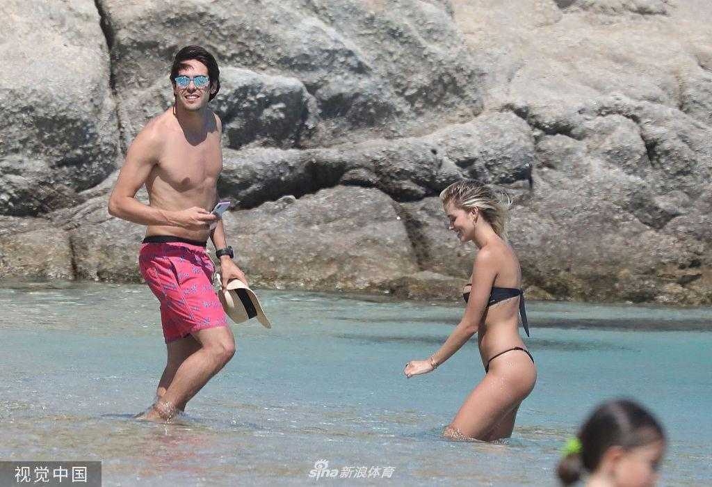 夕阳余晖下，卡卡和卡洛琳娜坐在海边的礁石上，两人共饮一杯鸡尾酒，剪影在金色的海面上显得格外宁静美好