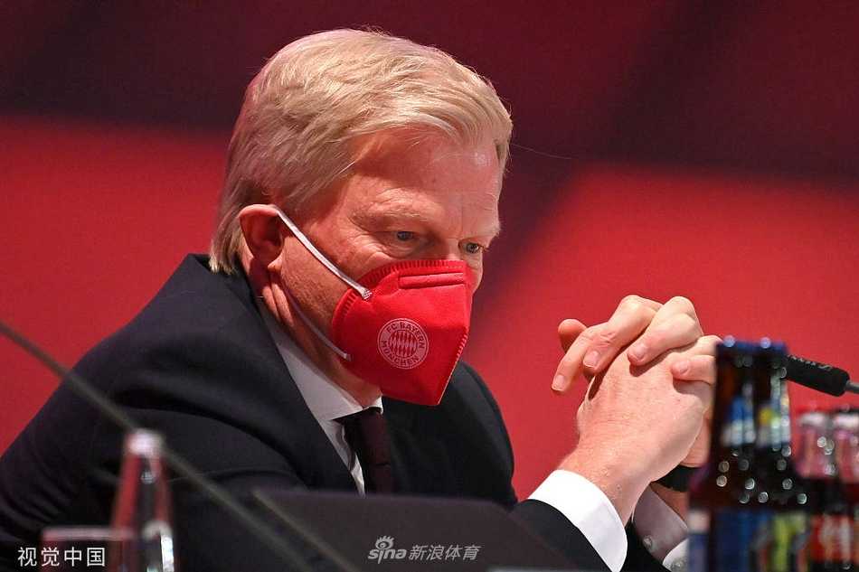 卡恩在一位愤怒发言的会员面前眉头紧锁，指尖轻点桌面仿佛在思考如何回应这如潮水般的指责，桌上的矿泉水瓶映出会场的紧张倒影。