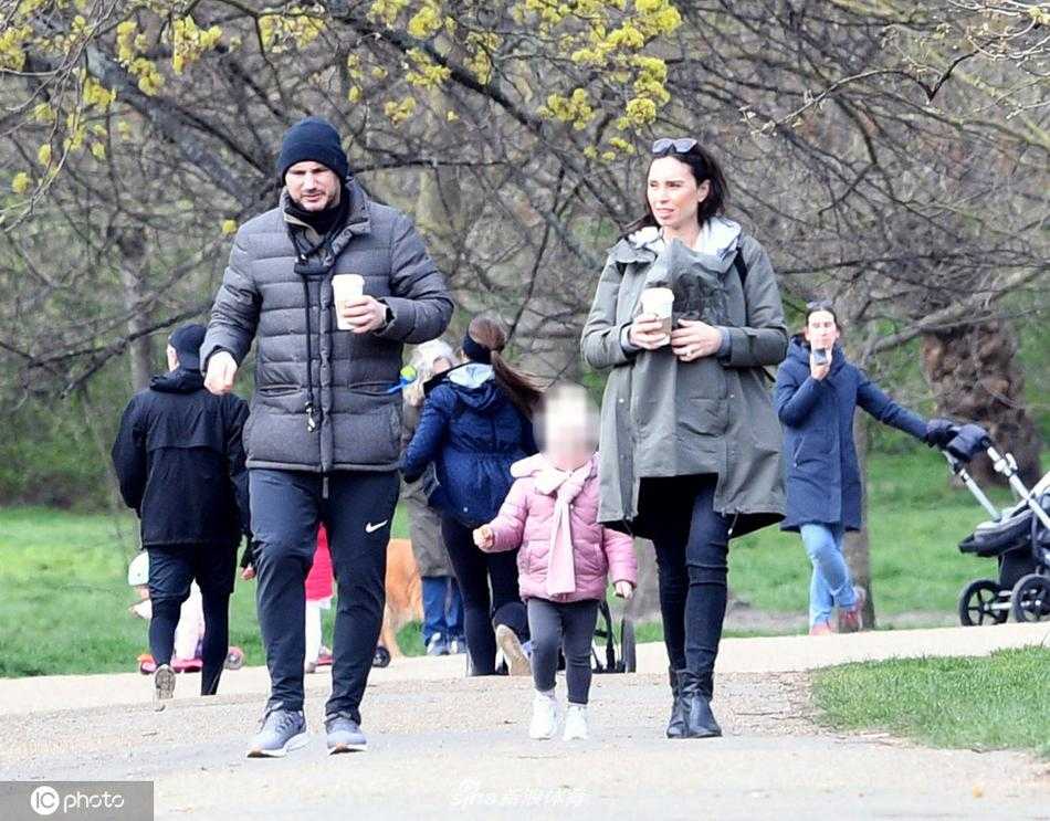 兰帕德穿着Nike运动裤和黑色羽绒马甲，一手牵着家人，一手拿着咖啡，脸上带着轻松惬意的笑容，完全摆脱了执教压力下的紧绷状态。