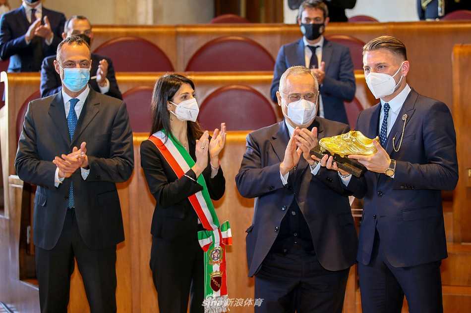 因莫比莱与妻子杰西卡在颁奖背景板前相视而笑，金靴奖杯在两人中间闪耀