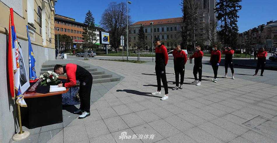 镜头拉远，整个足球场内气氛凝重，一面巨大的塞尔维亚国旗在看台上被球迷们缓缓传递展开，旗面上的国徽在阳光下熠熠生辉。场地中央，全体人员默哀肃立，安蒂奇的遗像静静面对着这片他曾深爱并为之奋斗的绿茵场，那一刻，时间仿佛凝固，只剩永恒的怀念。