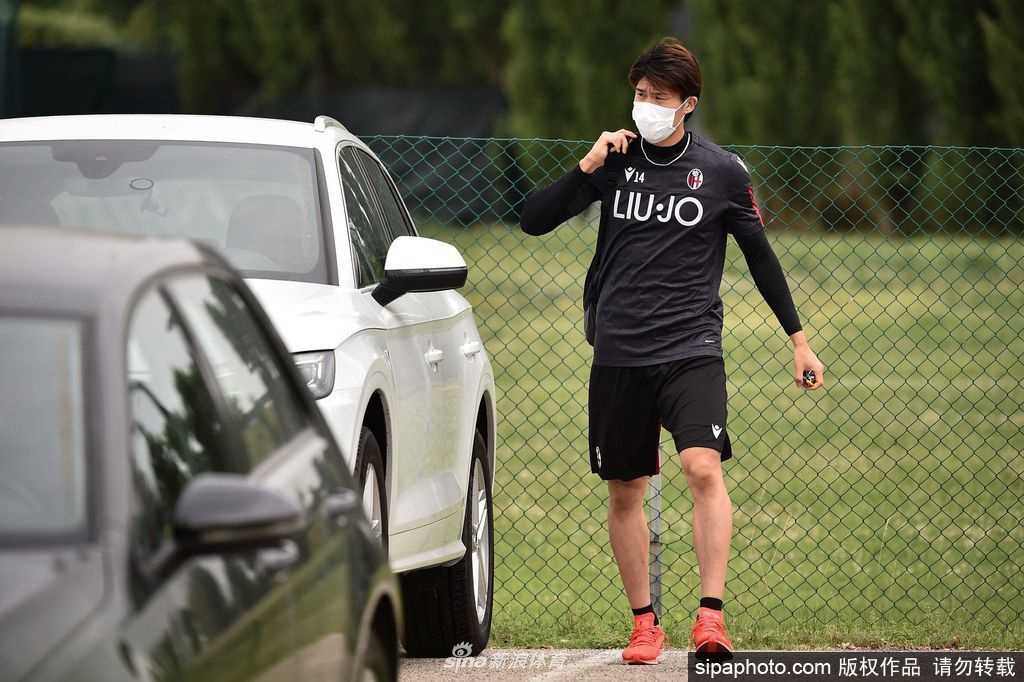 一名身穿博洛尼亚训练服的球员独自在空旷的训练场上带球，背后是看台的巨大阴影，整个画面充满了训练重启后的谨慎与疏离感。