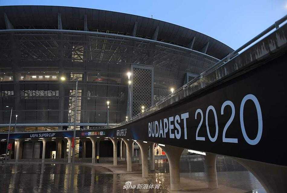 普斯卡什体育场雄伟的钢结构骨架在蓝天白云下勾勒出优雅的弧线，现代化的顶棚如同巨人的臂膀，温柔地环抱着这片即将上演龙争虎斗的绿茵场。