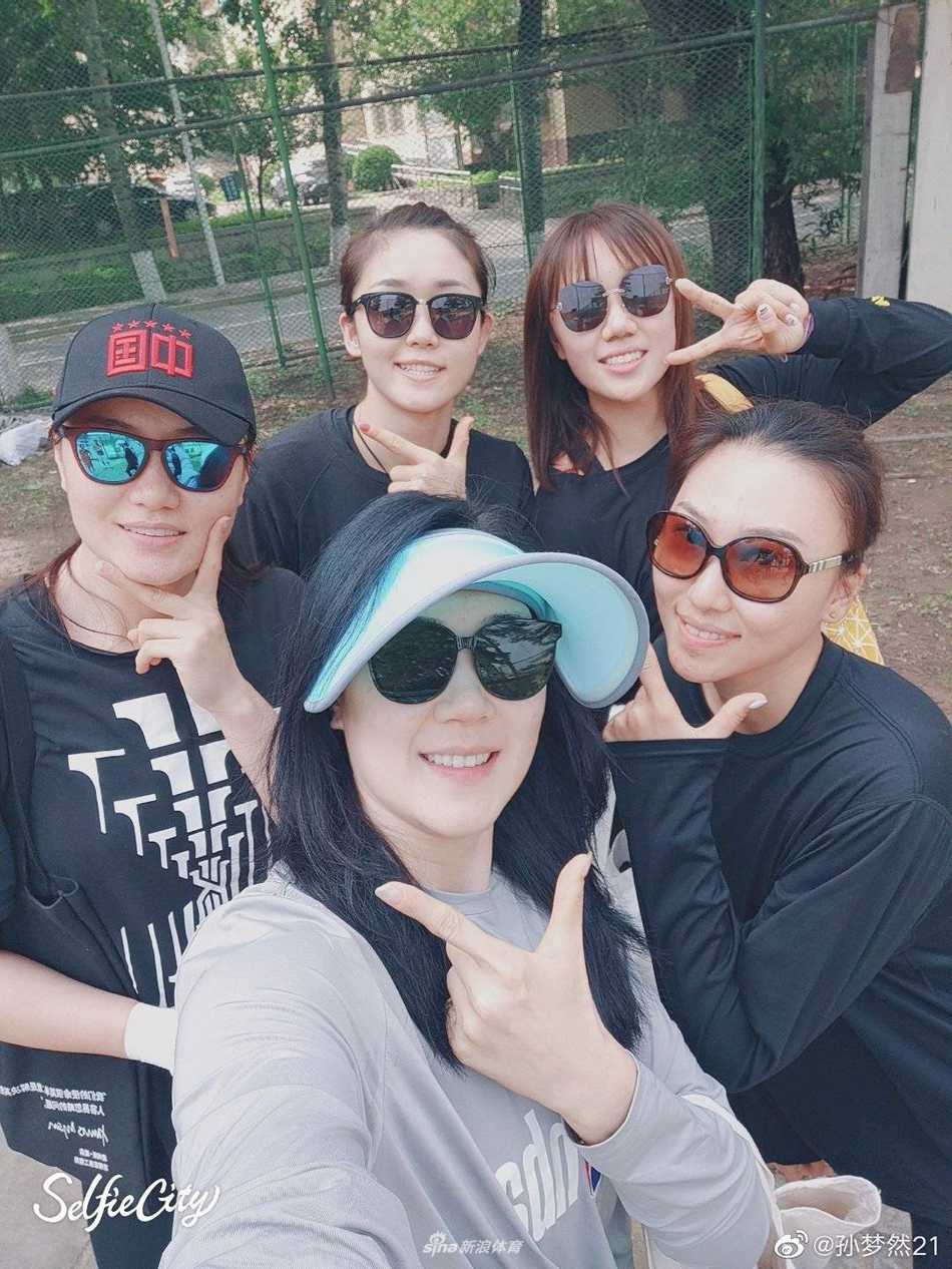 女篮领队孙梦然携队友“沙场”点兵 跨界玩票也要打出名堂 孙梦然坐在沙滩上开怀大笑,露出了洁白的牙齿,脸上的汗水在阳光下闪闪发光,她用手擦拭着额头,身后是队友嬉戏的身影,整个画面充满了青春的朝气和运动的快乐。