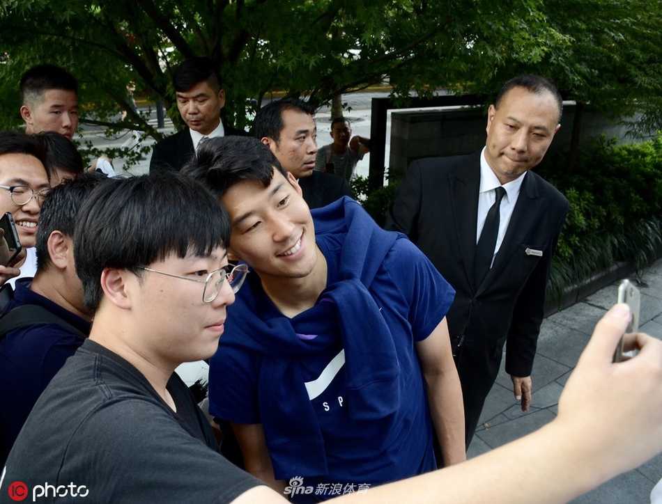 孙兴慜与几位女球迷合影，他微微弯腰配合镜头，右手比出可爱的爱心手势，亲和力瞬间拉满