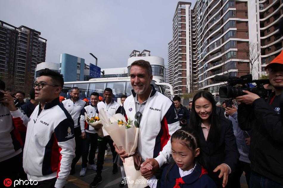 忧郁王子罗伯特·巴乔面露亲切微笑，耐心地为身边热情的中国小球迷在足球上签名，眼神中满是对后辈的鼓励。