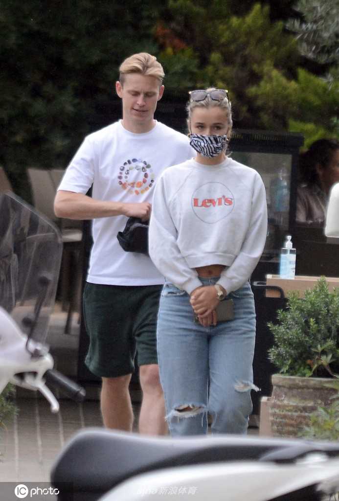 德容面带温柔笑意望向女友，而女友则低头查看菜单，桌上摆放的玻璃杯折射出午后阳光，气氛宁静而美好