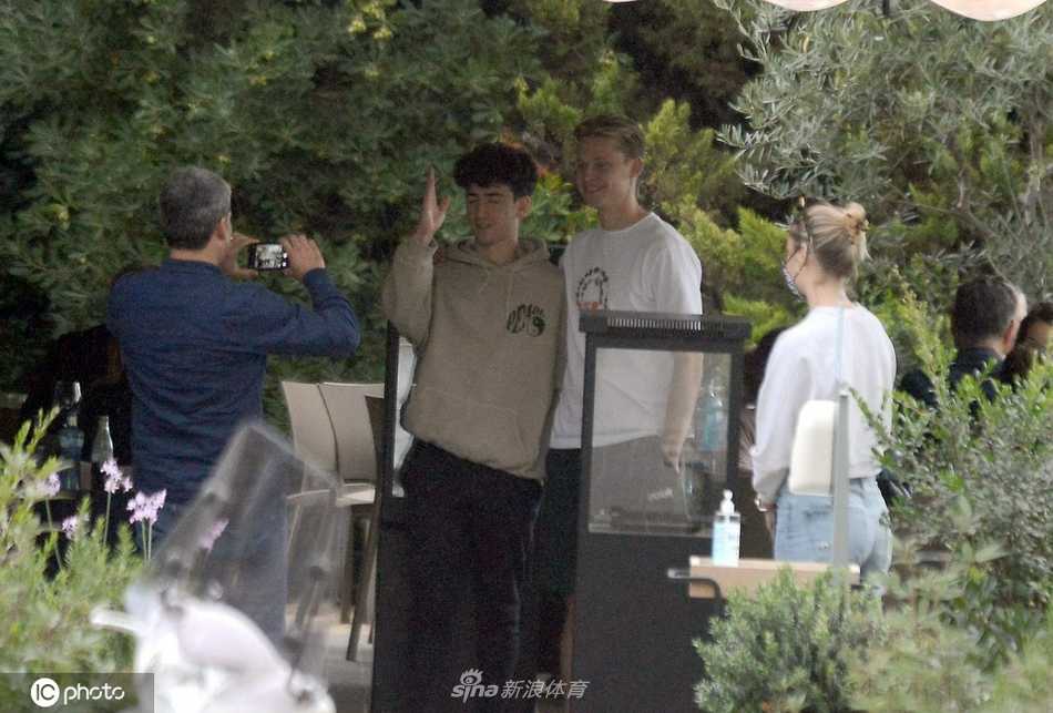 德容和女友并肩而坐，他侧身靠近女友耳边低语，似乎在分享一个有趣的故事，女友脸上随即浮现出浅浅的笑意