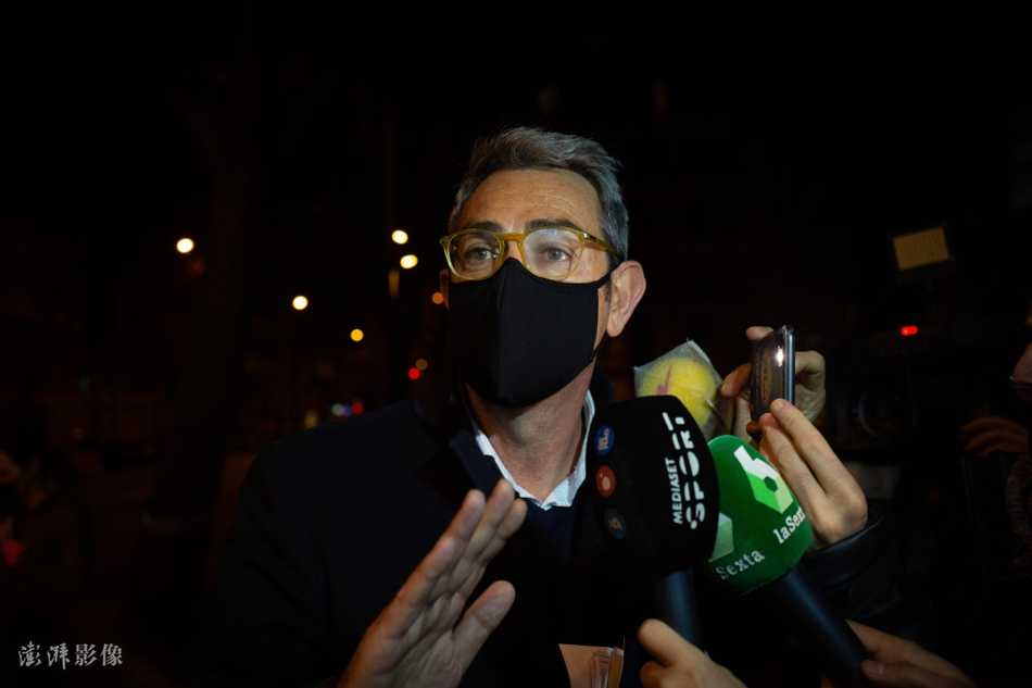 透过模糊的玻璃窗，可以看到一名全副武装的警员站在巴塞罗那办公室内部，警惕地注视着外面。他的身影与墙上巨大的队徽形成鲜明对比，象征着法律与俱乐部荣誉在此刻的狭路相逢。