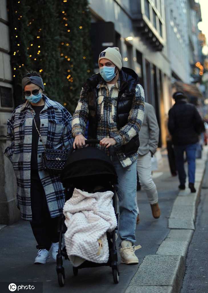 恰尔汗奥卢身穿深色羽绒服走在米兰街头，他的妻子辛雅娜推着婴儿车并肩而行，两人的目光温柔地落在孩子身上，温馨的氛围溢于言表。