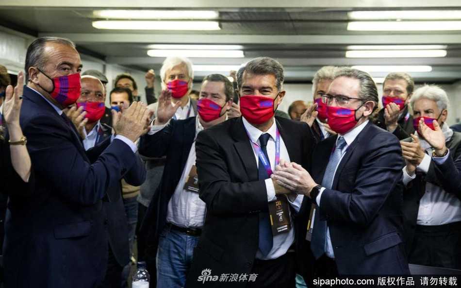 神情专注的拉波尔塔在堆满文件的办公桌前签署就职相关文件，身后巨大的巴萨队徽在灯光下格外醒目，暗示着他肩负的厚重历史使命与紧迫现实的艰难交织。
