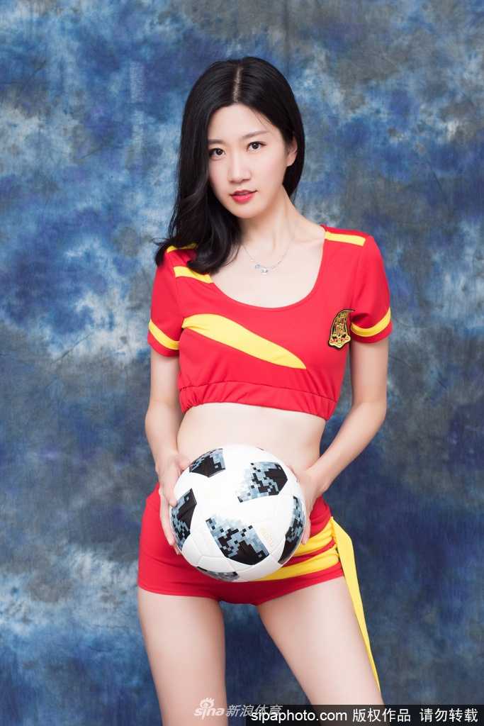 绿草如茵的背景下，宝贝侧身而坐，红色球衣与蓝色牛仔短裤的搭配充满活力，她望向远方，仿佛在眺望胜利的方向