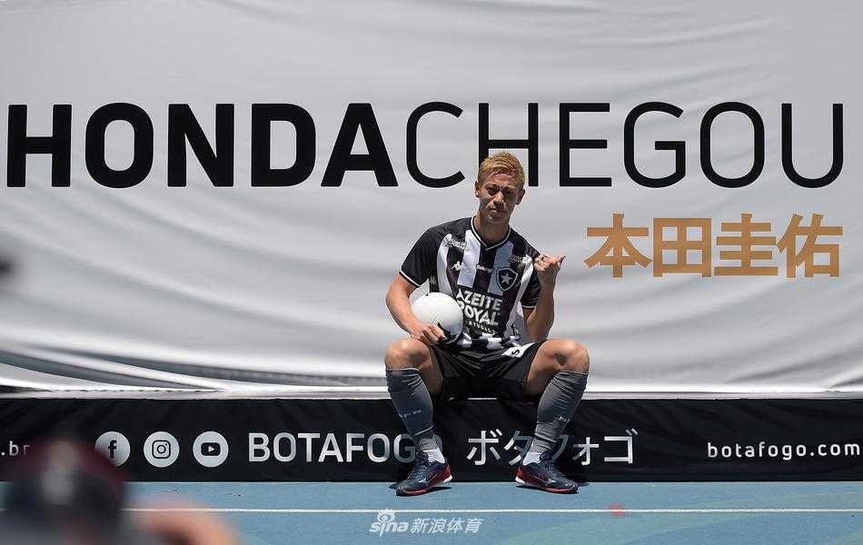 亮相仪式中的本田圭佑面对镜头比出招牌手势，面带自信微笑，身后的博塔弗戈队旗随风飘扬，象征着一段全新冒险的开始