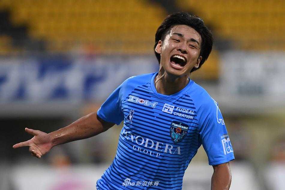 横滨FC球员在客场取胜后，兴奋地围成一圈，跳跃着庆祝他们重返J1联赛后的首场胜利，脸上的笑容如同当晚日立台球场的灯光一样灿烂。