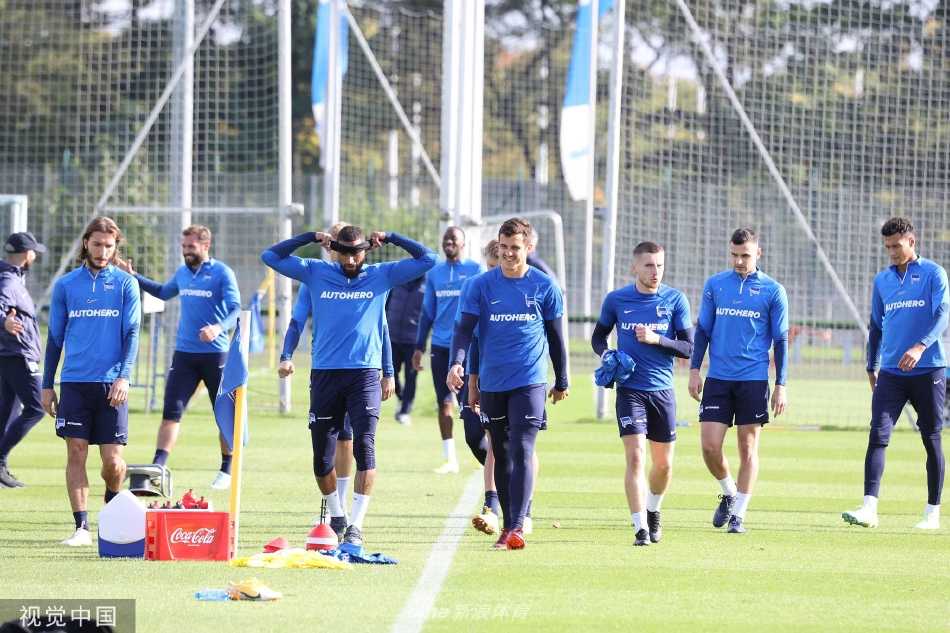两名中场球员在对抗训练中激烈拼抢，足球悬停在两人争抢的脚尖之上，背景是其他专注训练的队友，瞬间定格了训练的强度与激情。