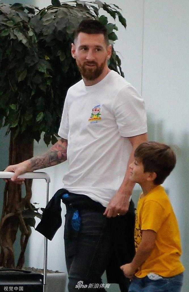 梅西注视着正在领取行李的家人，他的络腮胡在机场灯光下显得格外有型，一身休闲装束难掩其从容自信的巨星气质，同时眼神中又充满了对家人的关切。
