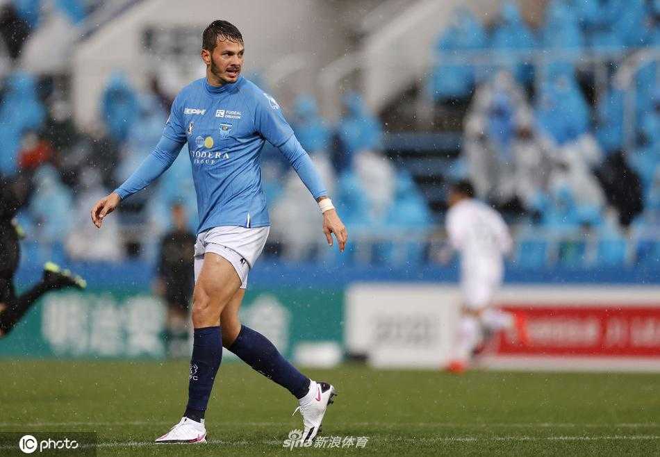 横滨FC前锋克莱伯在对方禁区内高高跃起争抢头球，他与大阪樱花后卫身体对抗激烈，展现了比赛的胶着与力量感。