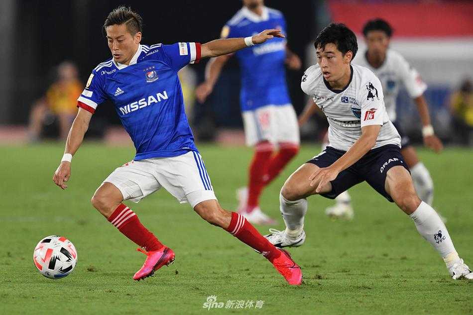 横滨FC的防守球员奋力滑铲，试图阻挡横滨水手队仲川辉人的突破，草屑飞溅，对抗激烈