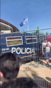 动态画面中，一位身穿利物浦球衣的球迷正试图与站在门口的警察交涉，下一秒，警棍便重重地挥向他的头部。
