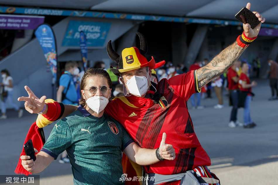 两位比利时女球迷在脸颊上精心绘制了比利时国旗和红魔元素的彩绘，她们的金发在阳光下闪闪发光，头戴着红魔主题的发饰，对着镜头摆出俏皮的姿势，将女性球迷的柔美与对足球的狂热完美融合。