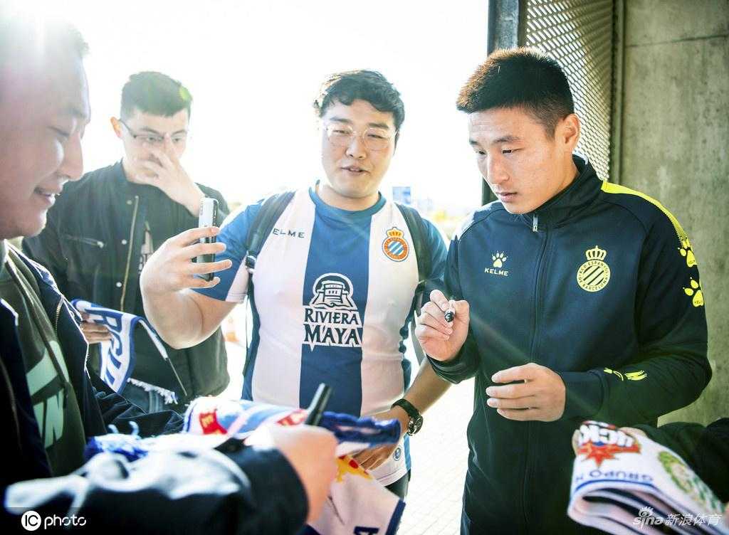 一位穿着武磊同款训练服的小球迷，正专注地等待武磊在自己的西班牙人队队旗上签名，画面充满温馨与传承的意味