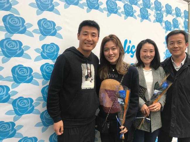 在装饰着彩带与圣乔治旗帜的街道上，武磊与妻子相视而笑，妻子怀中的蓝色玫瑰在阳光下闪烁着绸缎般的光泽，背景中熙攘的人群仿佛都成了这对恩爱夫妻的温馨背景板。