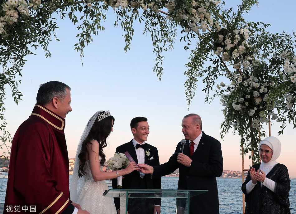 浪漫海岸见证幸福:厄齐尔大婚,总统亲临送祝福 厄齐尔与新娘阿米娜在蔚蓝海岸边甜蜜拥吻,身后是波光粼粼的海面和绚丽的晚霞,幸福洋溢在他们的脸上。