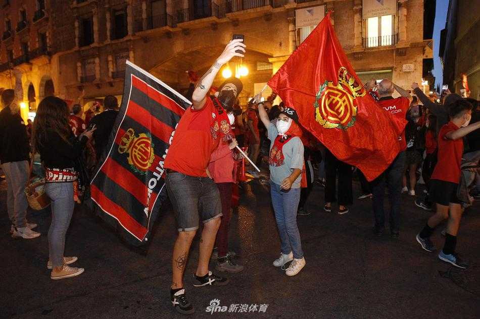 在狭窄的古老街巷中，一位年轻的球迷成为了画面的焦点。他的脸庞被红色的烟雾弹映得通红，紧握拳头的他张大嘴巴发出无声的呐喊，青筋微露的脖颈诉说着内心的狂喜。背景中虚化的人群和弥漫的烟雾，让这份属于个体的激情显得无比真实而强烈。