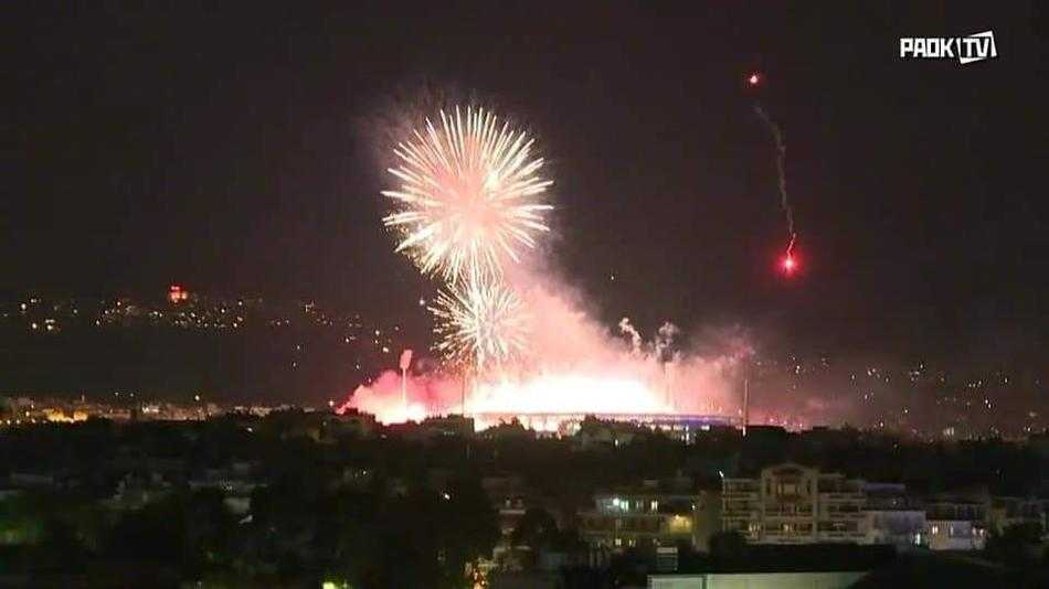 从高处俯瞰塞萨洛尼基的滨海大道，庆祝的人群高举烟火排成蜿蜒长队，星星点点的火光串联成一条流动的红色巨龙，沿着海岸线盘旋舞动，场面极为震撼壮观。