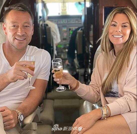 特里与爱妻托尼在私人飞机舱内高举香槟杯，两人面带微笑深情对视，窗外是万里无云的碧蓝天空，金色的阳光洒在晶莹的香槟杯上，折射出胜利的喜悦。