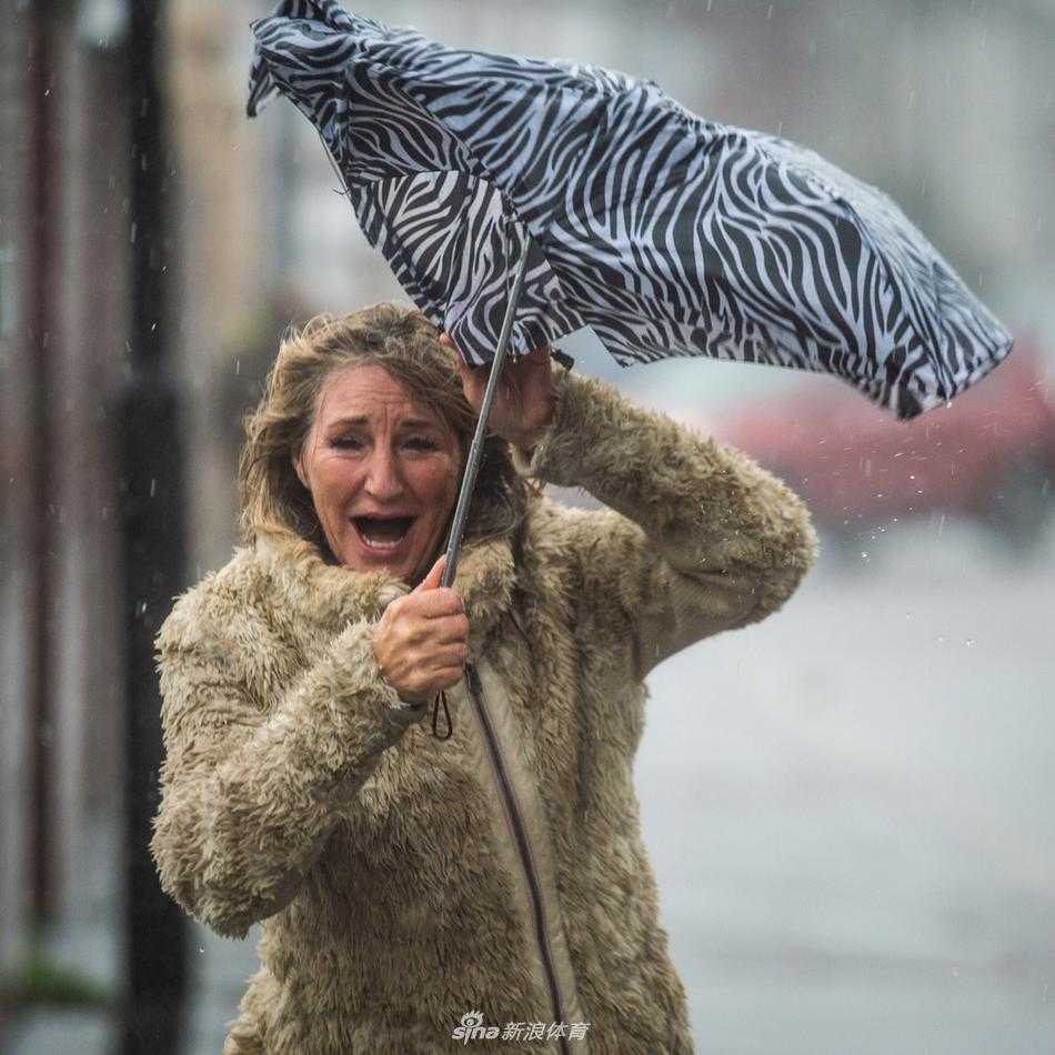瓢泼大雨如注而下，一位谢菲尔德联队的铁杆球迷身披雨衣，但他的脸庞已被雨水打湿，他神情专注而坚定地望向球场方向，手中的围巾在风雨中猎猎作响，仿佛一面不倒的爱的旗帜。