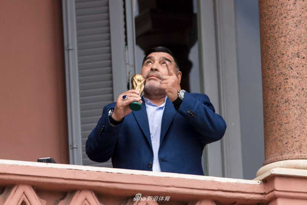 镜头拉近，总统府的会客厅内，马拉多纳与费尔南德斯并肩而坐，身前桌上摆满了阿根廷国家队的球衣。两人神情专注地交谈着，马拉多纳用手势强调着什么，似乎正在向总统勾勒一个关于阿根廷足球未来的蓝图。