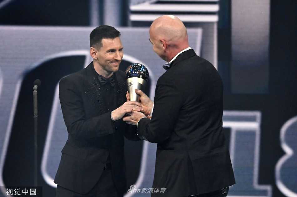 梅西高举奖杯向全场致意，银色西装映衬着金色 trophy，他身后的国际足联标志宛若王座，这一刻他是足球王国当之无愧的君主