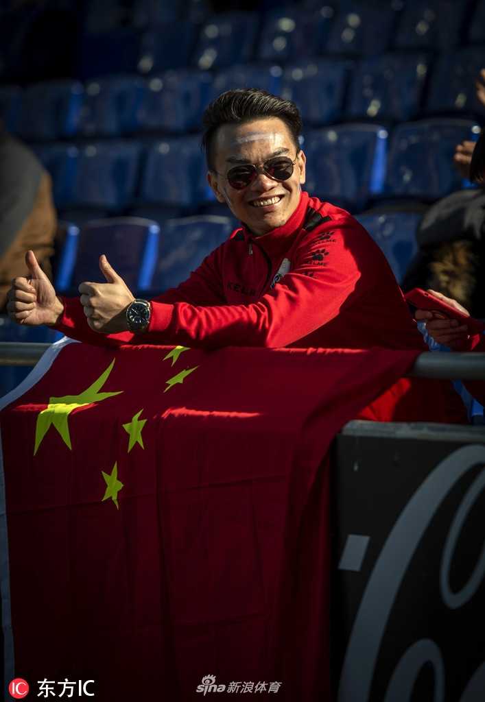 一位身穿武磊球衣的中国小球迷坐在父亲的肩头，小手紧紧握着一面小国旗。孩子清澈的眼神望向球场中央，那里有他心中的英雄——武磊，正在为梦想而战。