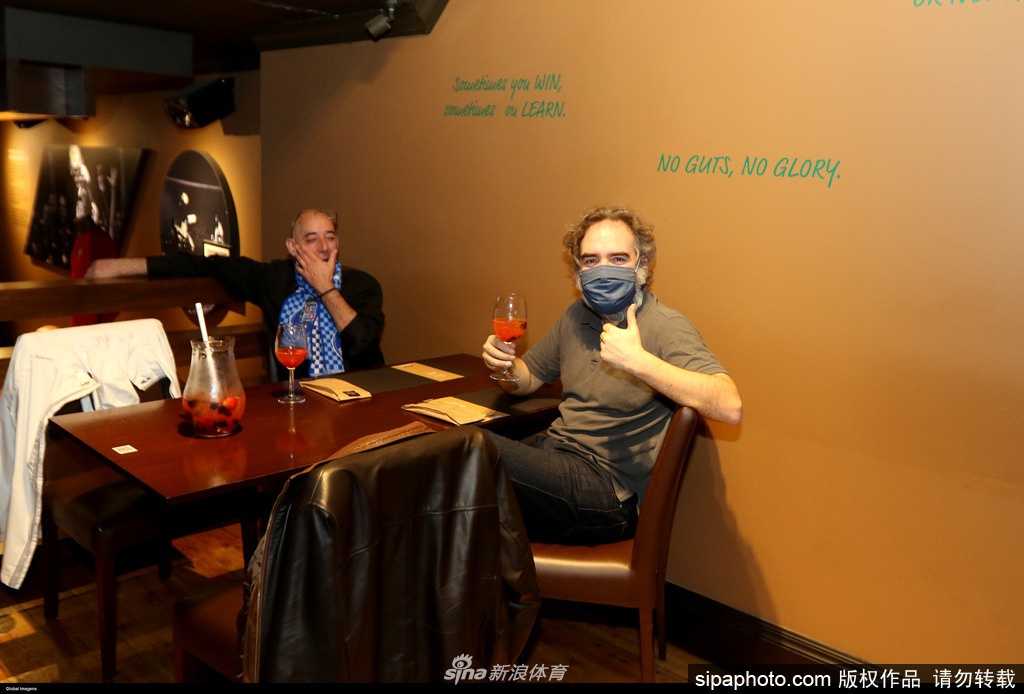 在葡萄牙的一家酒吧内，身穿波尔图蓝色球衣的球迷们肩并肩站在一起，他们脸上戴着口罩，但眼神专注地盯着电视屏幕，仿佛置身于球场看台一般。酒杯和零食散落在桌上，记录着这个因疫情而变得特殊的观赛之夜。
