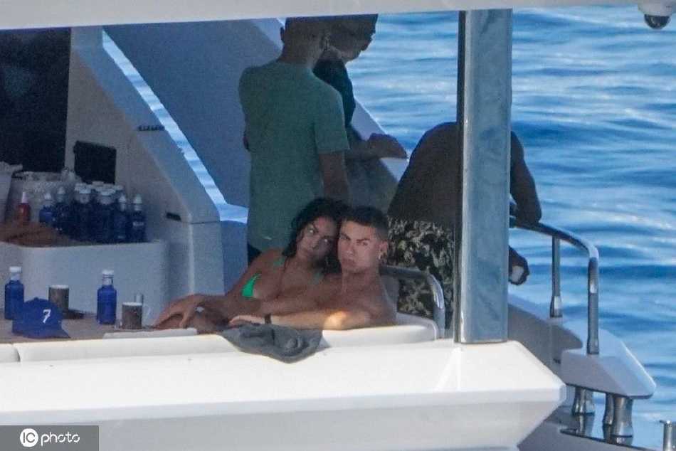 C罗与乔治娜在游艇甲板上亲密相拥，碧蓝海水与白色游艇构成浪漫背景，两人笑容灿烂尽显度假好心情