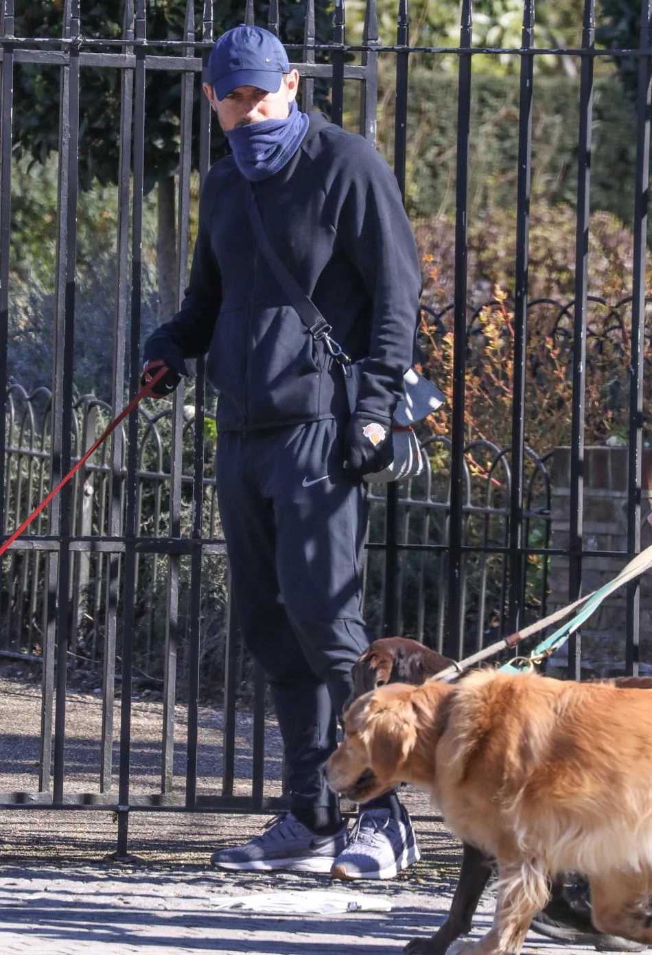 兰帕德牵着爱犬走在居民区的小路上，手里还拿着一个蓝色的袋子，他戴着普通手套，但这显然不是用于防护的一次性医用手套