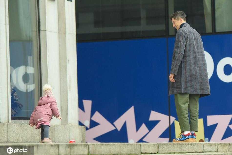 莱万与妻子安娜并肩走在华沙街头，两人穿着休闲冬装，如同普通情侣般低声交谈。莱万侧身倾听妻子说话，安娜脸上洋溢着轻松的笑容，两人身后是冬日城市斑驳的光影。